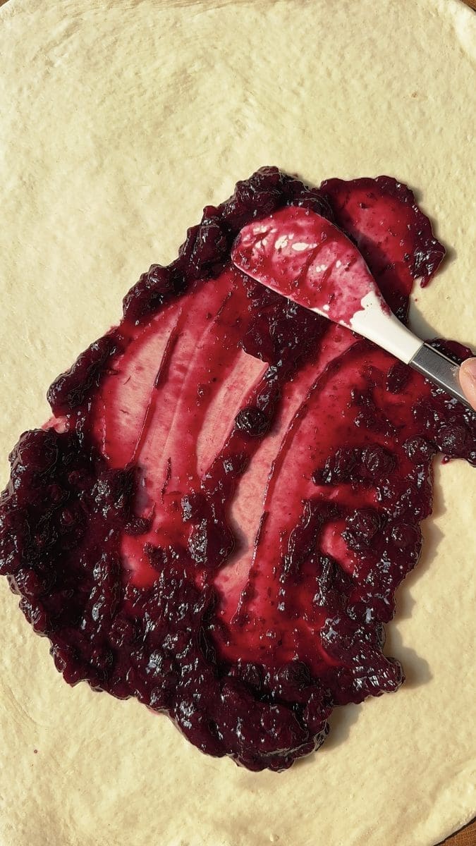 Spreading blueberry jam over the dough.