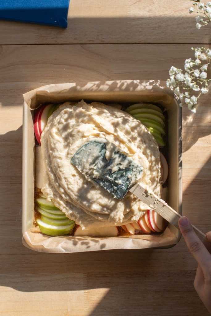 Spreading the cake batter over the apples in the pan.