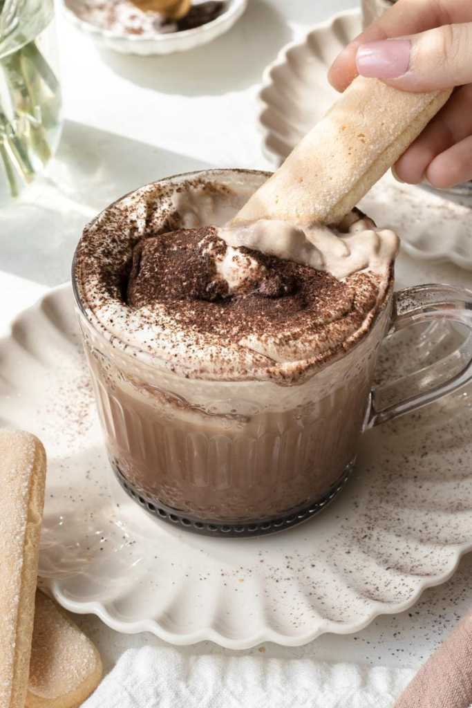 dipping a ladyfinger biscuit into the mascarpone whipped cream on top of the tiramisu latte