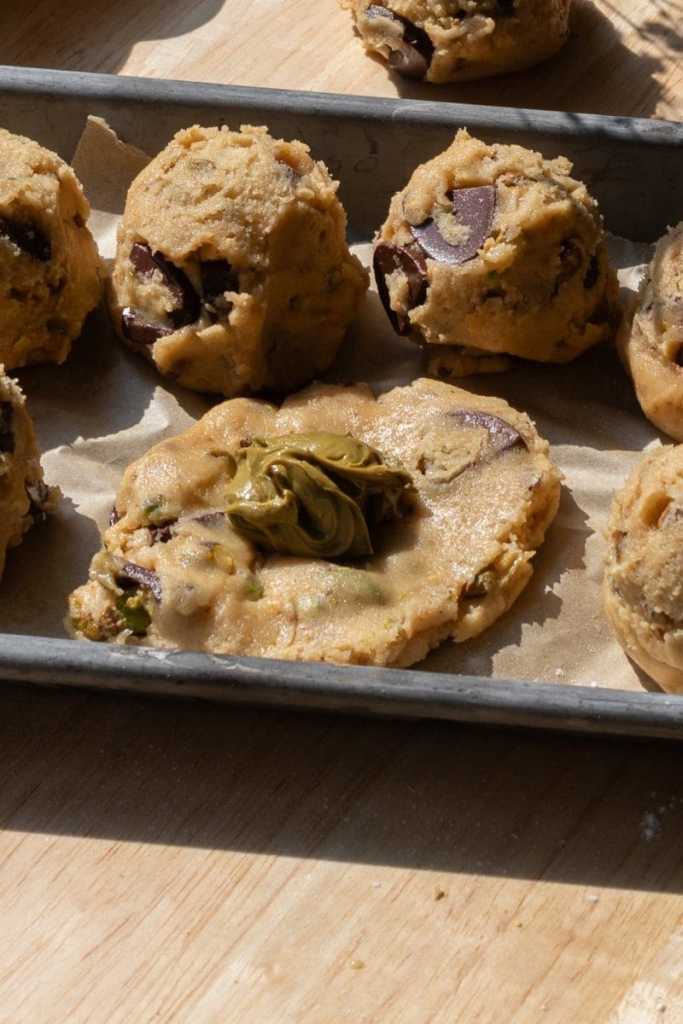 A cookie dough ball flattened out with a scoop of pistachio cream on top of it.