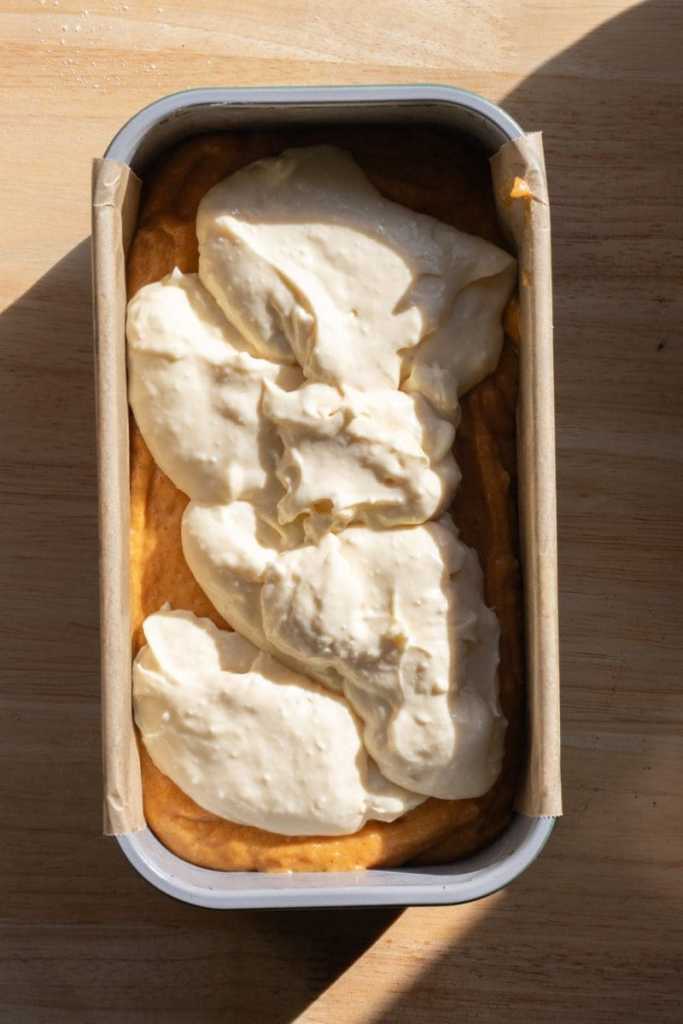 Cream cheese filling on top of the pumpkin batter in a loaf pan.