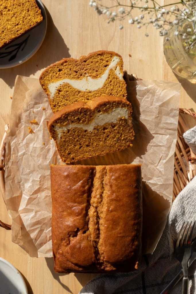 Two slices of the cream cheese swirl pumpkin bread sliced and laying on each other next to the full loaf.