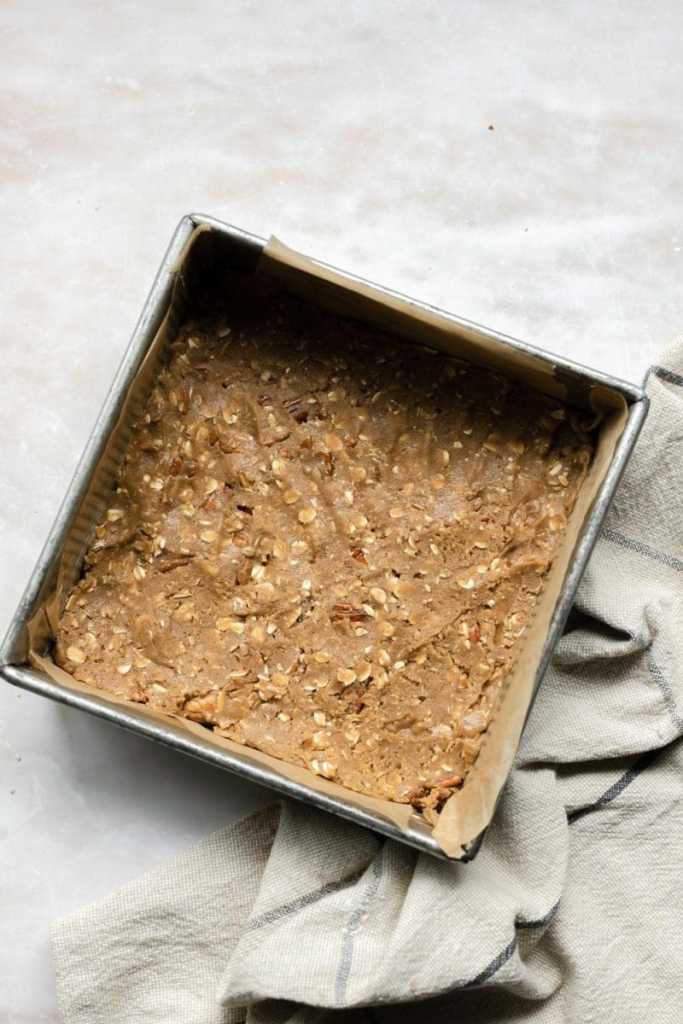 The cookie dough in a flat layer in a square pan.