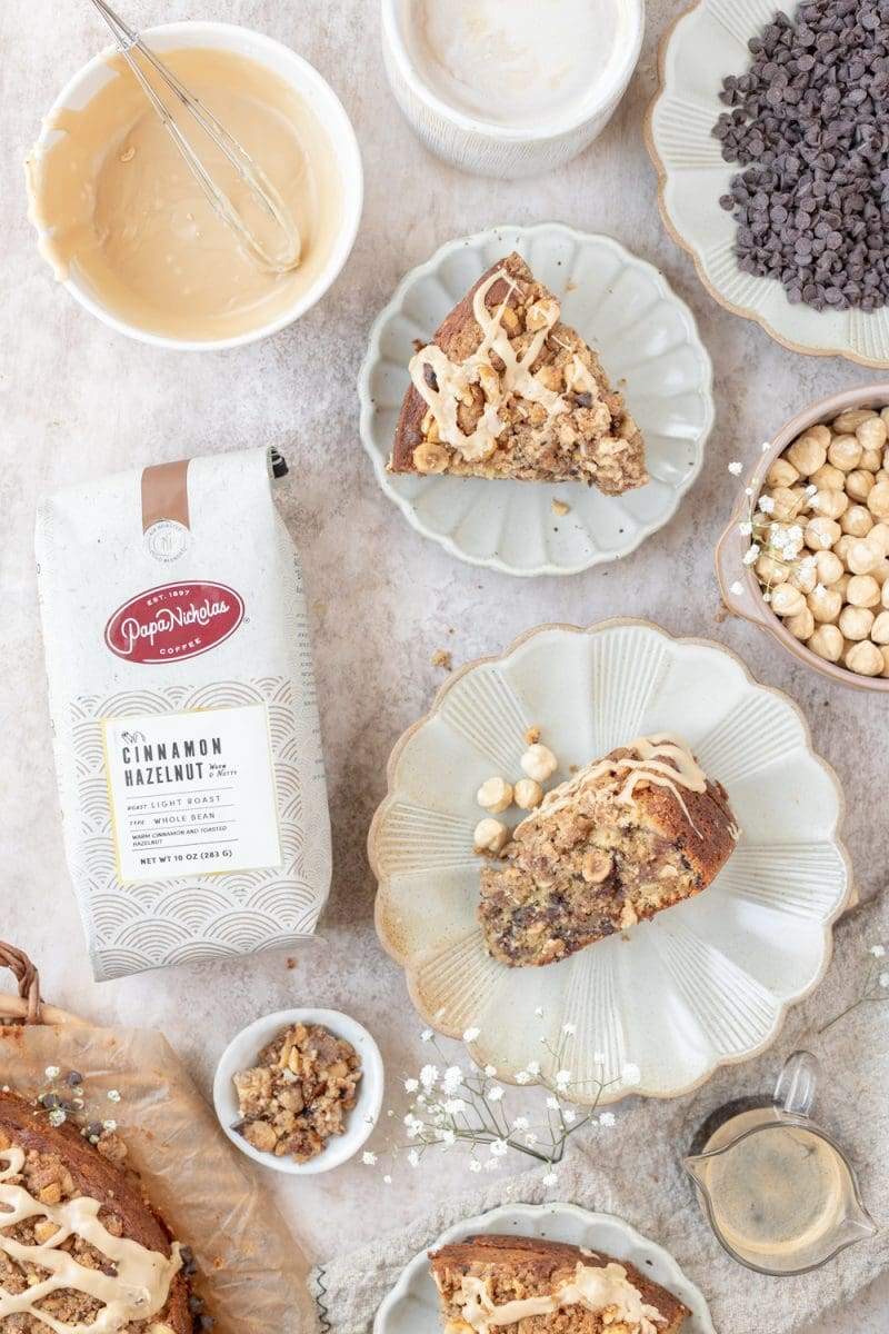 a stylized flat lay of the hazelnut chocolate chip coffee cake, with slices on different scalloped plates next to a bag of PapaNicholas Coffee.
