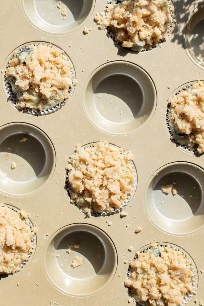 The muffins, topped with streusel, distributed in a muffin pan.