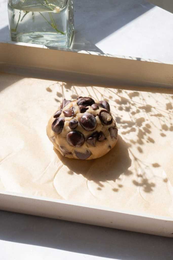 The single chocolate chip cookie dough ball on a parchment lined baking sheet, before baking.