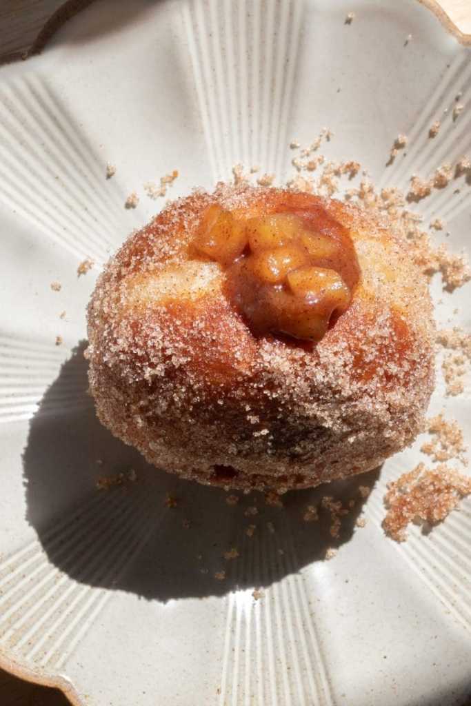 Close up of a filled apple pie brioche donut on a plate.