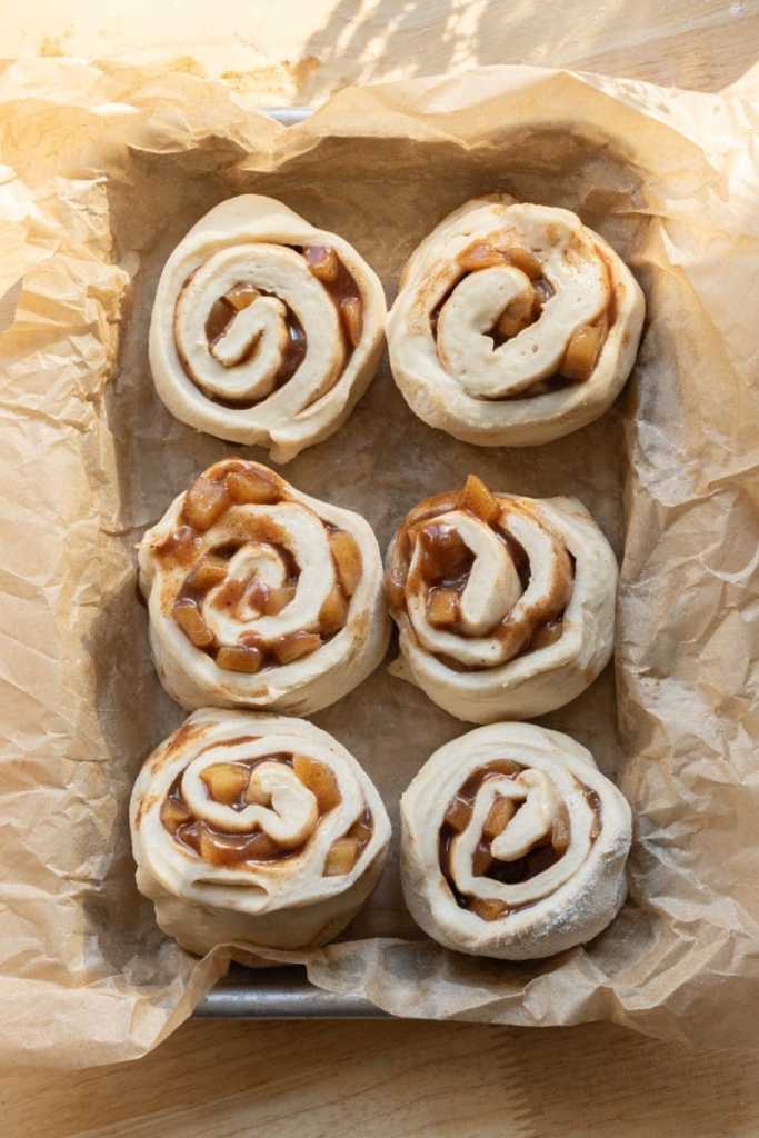 The apple pie cinnamon rolls sliced and rising in a baking tray.