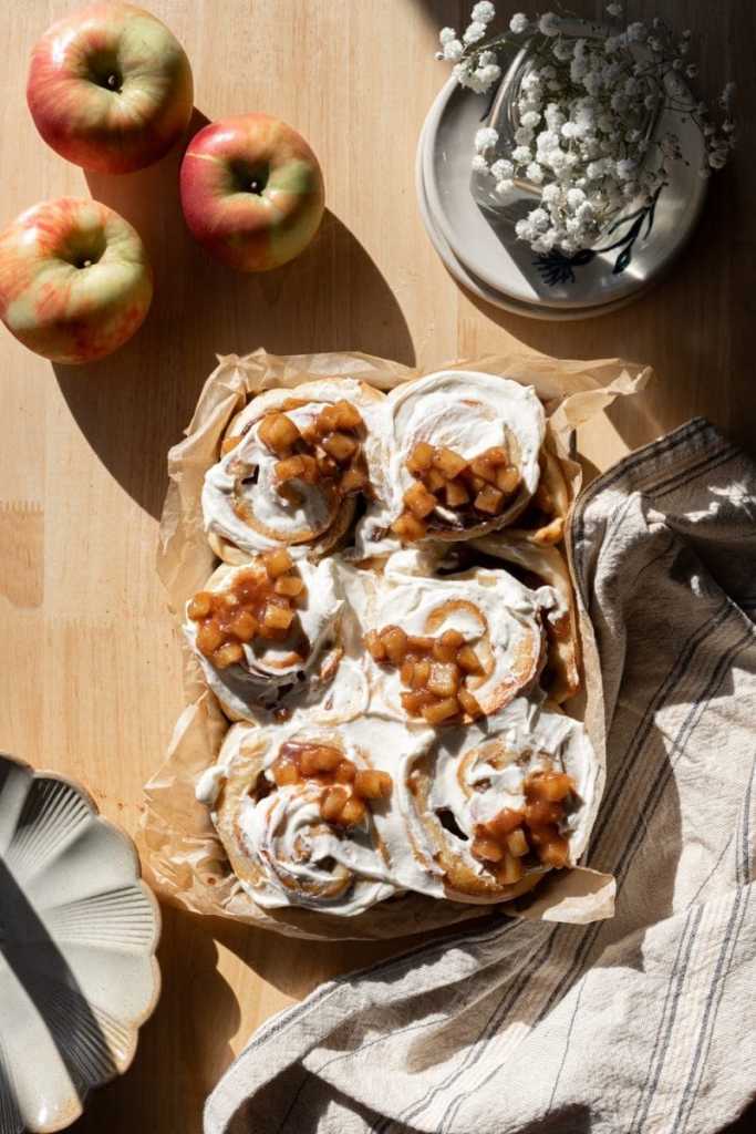 The frosted apple pie cinnamon rolls in a baking tray.