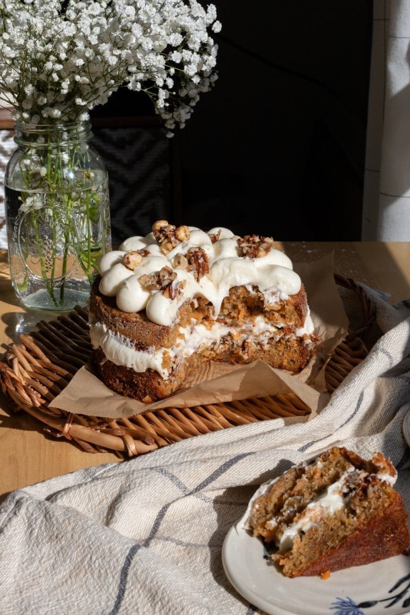 The sliced  carrot cake with honey praline, with a slice of cake laying down in front of the whole cake.