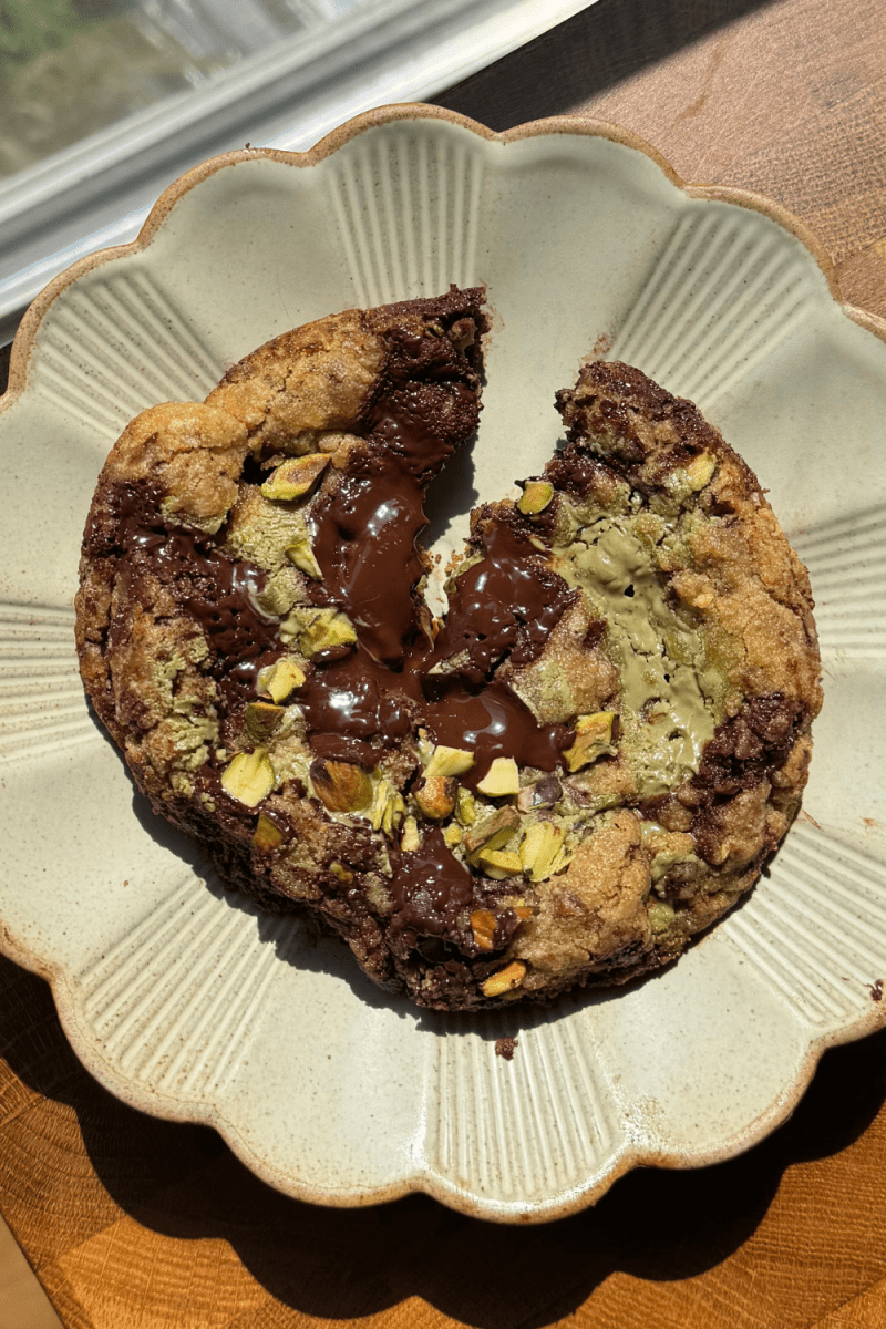 The single serve pistachio cream chocolate chip cookie cut in half on a plate.